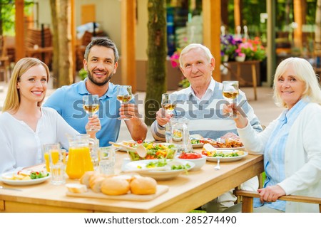 Cheers! Happy young and senior couples sitting at the dining table and toasting with wine