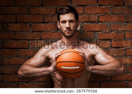 Are you ready to play? Confident young muscular man holding basketball ball while standing against brick wall