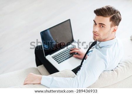 Confident businessman at work. Top view of confident young man working on laptop while sitting on sofa