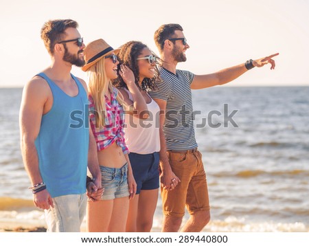 Enjoying carefree time with friends. Group of young cheerful people walking together along the beach and smiling while one man pointing