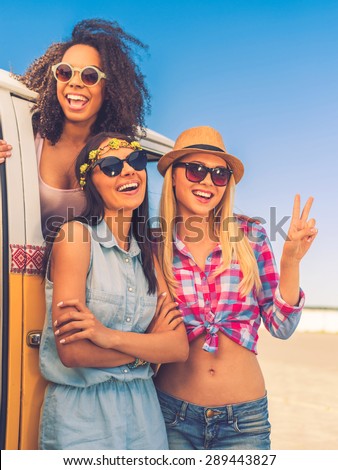 Carefree time with friends. Happy young African woman looking out from the retro minivan while two her friends standing near her