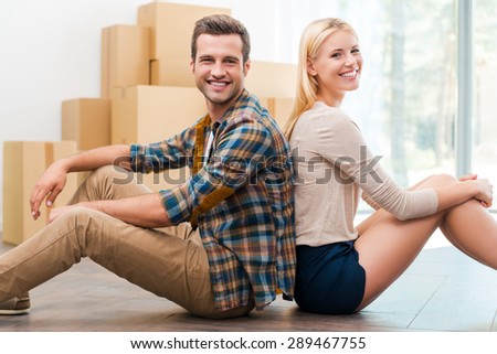 Just moved to their new apartment. Cheerful young couple sitting on the floor of their new apartment while cardboard boxes laying in the background
