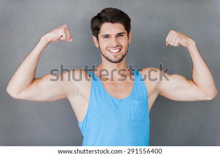 True masculinity. Handsome young muscular man showing his perfect biceps while standing against grey background