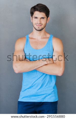 Confident in his perfect shape.Handsome young muscular man holding arms crossed while standing against grey background