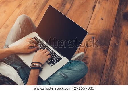 Man surfing the net. Top view of man working on laptop while sitting on the wooden floor