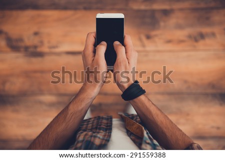 Staying in touch. Top view of man holding smart phone while standing on the wooden floor