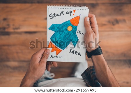 Your dreams may come true. Top view of man holding note pad with drawing on it while standing on the wooden floor