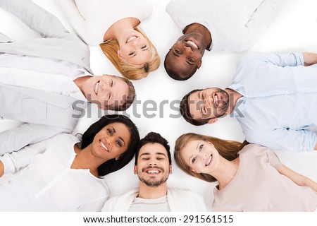 Together we are stronger. Top view of cheerful group of multi-ethnic people laying on their backs and smiling while standing isolated on white