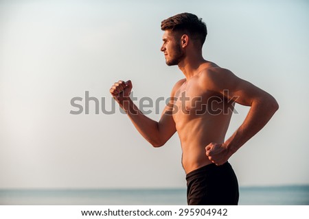 Energy inside him. Side view of confident young muscular man running along the seaside