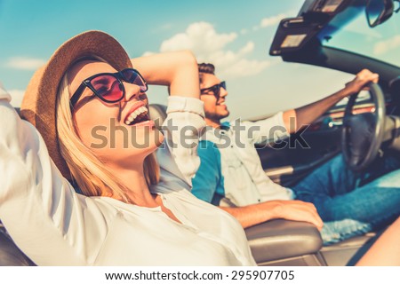 Freedom of the open road. Side view of joyful young woman relaxing on the front seat while her boyfriend sitting near and driving their convertible