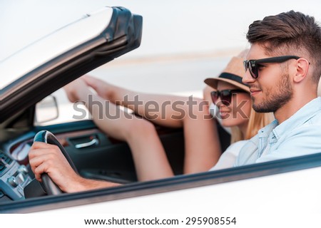 Relaxing during road trip. Beautiful young couple smiling and looking forward while riding in their white convertible