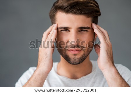 Feeling headache. Depressed young man touching his head and expressing negativity while standing against grey background
