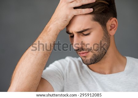 Failed again. Depressed young man touching his head and expressing negativity while standing against grey background