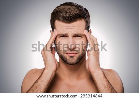 Feeling headache. Portrait of frustrated young shirtless man looking at camera and touching head with hands while standing against grey background