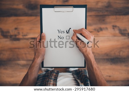 Making a right choice. Top view of man making a check mark in clipboard while standing on the wooden floor