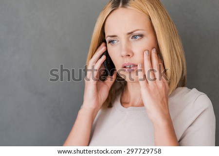 She just got bad news. Frustrated mature woman talking on the mobile phone and expressing negativity while standing against grey background