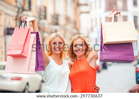 Look what we got! Joyful mature woman and her daughter stretching out shopping bags and looking at camera while standing outdoors
