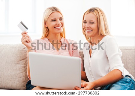 Online shopping makes life easier. Cheerful young woman and her mother shopping through Internet while sitting on sofa