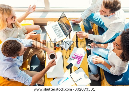 Working together for better results. Top view of four happy young people working together while sitting at the wooden desk in office