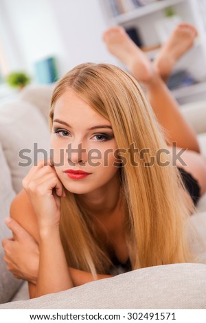 Lazy day on sofa. Confident young woman in lingerie looking at camera while lying on sofa