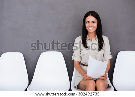 Successful job candidate. Confident young businesswoman holding paper while sitting on chair against grey background