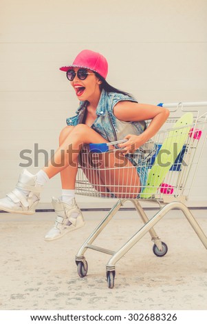 So young and carefree! Excited young woman expressing positivity while sitting in shopping cart against the garage door