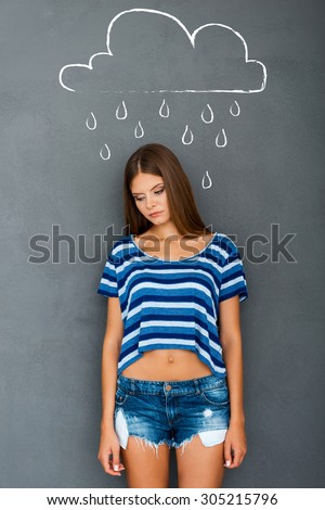 Feeling hopeless. Sad young woman looking down while standing against grey background with drawing upon her head