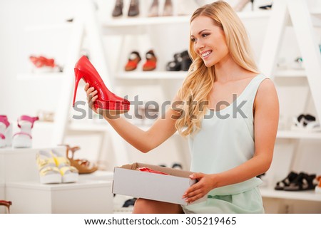 FInding the perfect pair! Smiling young woman taking red shoe from the box and looking at it while sitting in the shoe store