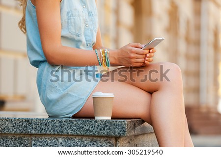 Urban connection. Close-up of young woman holding mobile phone while sitting outdoors