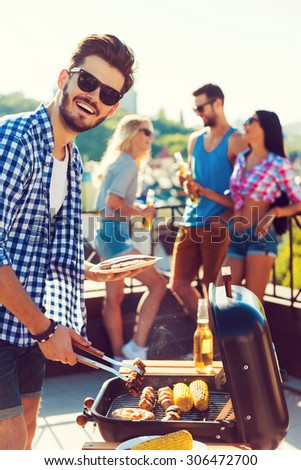 Tasty food and good company. Happy young man barbecuing and looking at camera while three people having fun in the background