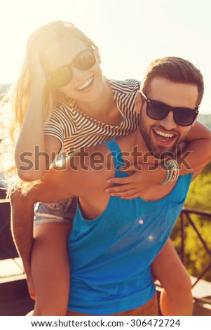 We love having fun. Happy young man carrying his girlfriend on the shoulders while having fun together on the roof
