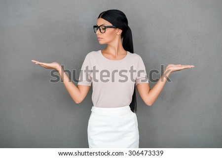 What to choose? Confident young businesswoman holding copy spaces on her hands while standing against grey background