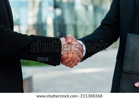 Sealing a deal. Close-up of two young businessmen shaking hands while standing outdoors