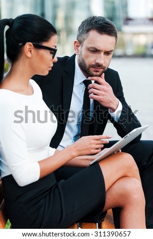 She needs an expert advice. Thoughtful young businessman holding hand on chin and looking at digital tablet while his female colleague pointing at it
