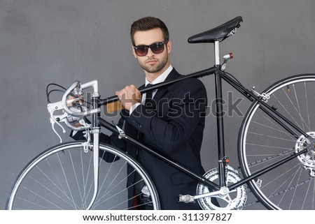 Perfect city transportation. Confident young businessman carrying his bicycle on shoulder while standing against grey background