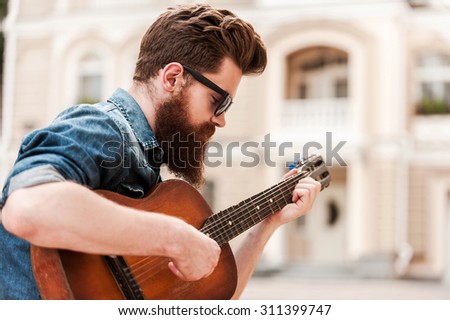 Intense guitar player. Young bearded man playing the guitar while sitting outdoors