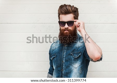 Rugged and manly. Confident young bearded man looking at camera and adjusting eyewear while standing outdoors