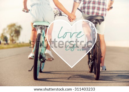Love is... Rear view of young couple holding hands while riding on bicycles along the road
