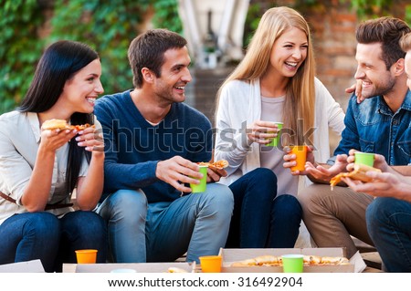 Spending good time with friends. Group of cheerful young people talking to each other and eating pizza while sitting outdoors