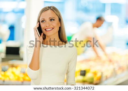What would you like for dinner? Happy young woman talking on the mobile phone and smiling while standing in a food store