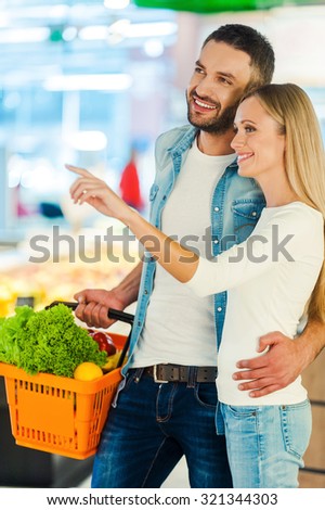 We should buy this! Cheerful young couple smiling and pointing away while standing in a food store