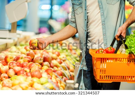 This should be fine. Close-up of young man holding apple and shopping bag while standing in a food store