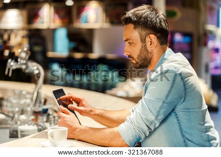 Surfing the net in bar. Side view of young man working on digital tablet while sitting at the bar counter