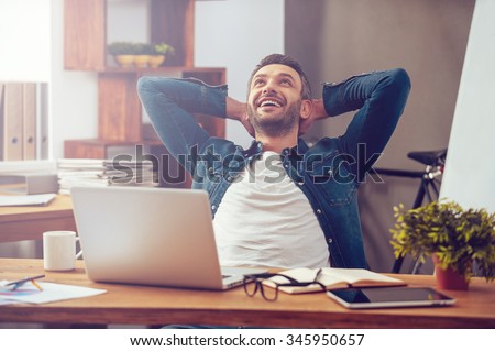 Photo of Satisfied with work done. Happy young man working on laptop while sitting at his working place in office