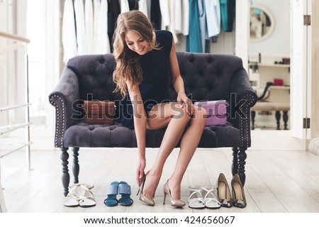 That is perfect pair! Beautiful young woman trying on high heel shoes while sitting on sofa at the shoe store 商業照片 © 