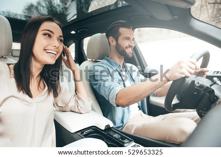 Enjoying travel. Beautiful young couple sitting on the front passenger seats and smiling while handsome man driving a car Foto stock © 