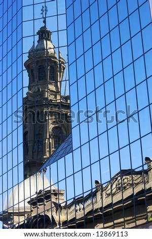 Church tower and roof mirrored in a modern glass office tower in downtown Santiago de Chile.