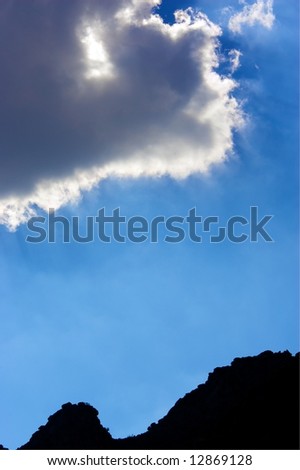 Cloud with the sun behind it against a blue sky with the curved silhouette of a hill.