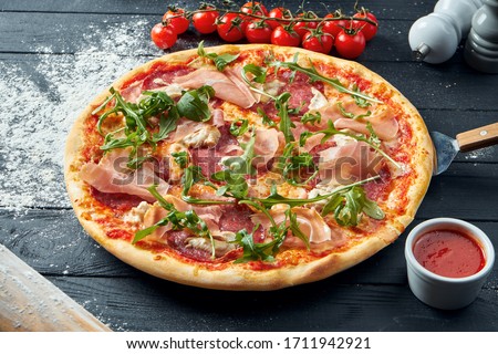 Baked pizza with salami, prosciutto and chicken with red sauce and melted cheese on a black wooden background in a composition with ingredients. Top view