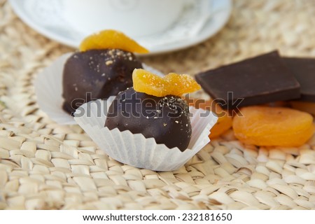 Handmade chocolate truffle with dried apricots on the woven surface. Dried apricots and pieces of black chocolate in the background